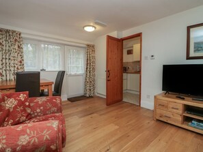Ein Wohnzimmer mit einer Couch, einem Fernseher, einem Holzkasten und einer Tür, die in eine Küche führt.