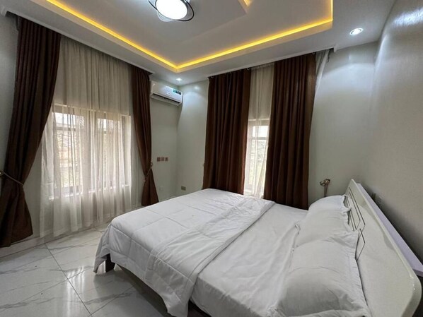 A bedroom with a bed, curtains, and a ceiling light fixture. - Treasure Court Apartment (Port Harcourt)