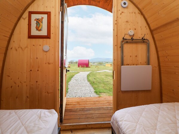 Eine Holzhütte mit einem Bett, einer zur Außenwelt führenden Tür und einem gerahmten Bild an der Wand.