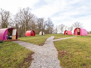Ein Campingplatz mit mehreren roten Zelten, die halbkreisförmig angeordnet sind, einem Kiesweg in der Mitte und kahlen Bäumen im Hintergrund.