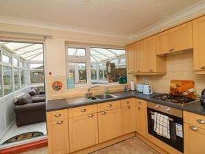 A kitchen with wooden cabinets, a gas stove, a sink, and a window overlooking a garden. - 5 Overstone Drive, Wisbech (Wisbech)