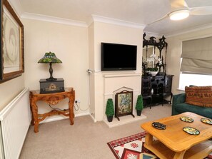 A living room with a television, a fireplace, a green sofa, a wooden coffee table, and a patterned rug. - 5 Overstone Drive, Wisbech (Wisbech)