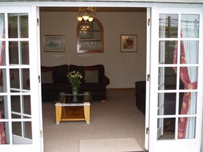 An open door leading to a living room with a sofa, a coffee table with a vase, and a chandelier. - Coach House 5, Perth (Perth)