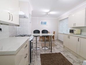 A modern kitchen with white cabinets, a gas stove, two bar stools, a dining table, and a microwave.