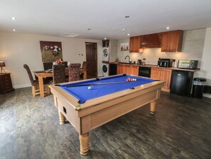 Une table de billard dans une pièce comprenant un coin cuisine, des meubles en bois et une table à manger avec des chaises.