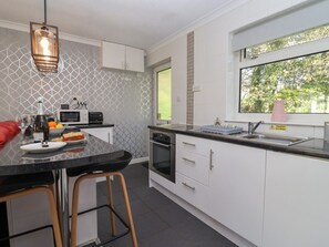 Une cuisine moderne avec des meubles blancs, un plan de travail noir et une fenêtre donnant sur un paysage verdoyant.