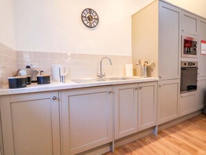 A kitchen with a sink, countertop, cabinets, a clock, and a microwave. - The Apple Store, Tarporley (Tarporley)
