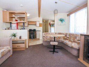 A modern living room with a sofa, a round table, and a kitchen in the background. - Hideaway Lodge, Abergele (Abergele)