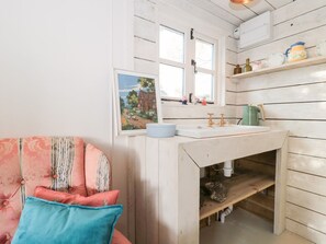 A rustic bathroom with a wooden vanity, a window, and a shelf with toiletries. - Shades Farm Summerhouse, Minety (Circenester)