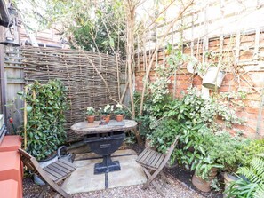 Eine Terrasse mit einem runden Tisch, zwei Holzstühlen und Blumentöpfen.