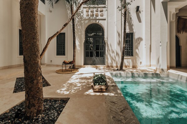 Une cour dotée d’une piscine, de palmiers et d’une arche de style traditionnel.