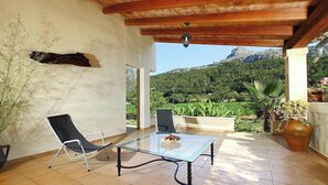 Un patio cubierto con una mesa de vidrio, dos sillas, un lámpara colgante y vistas a un paisaje montañoso.
