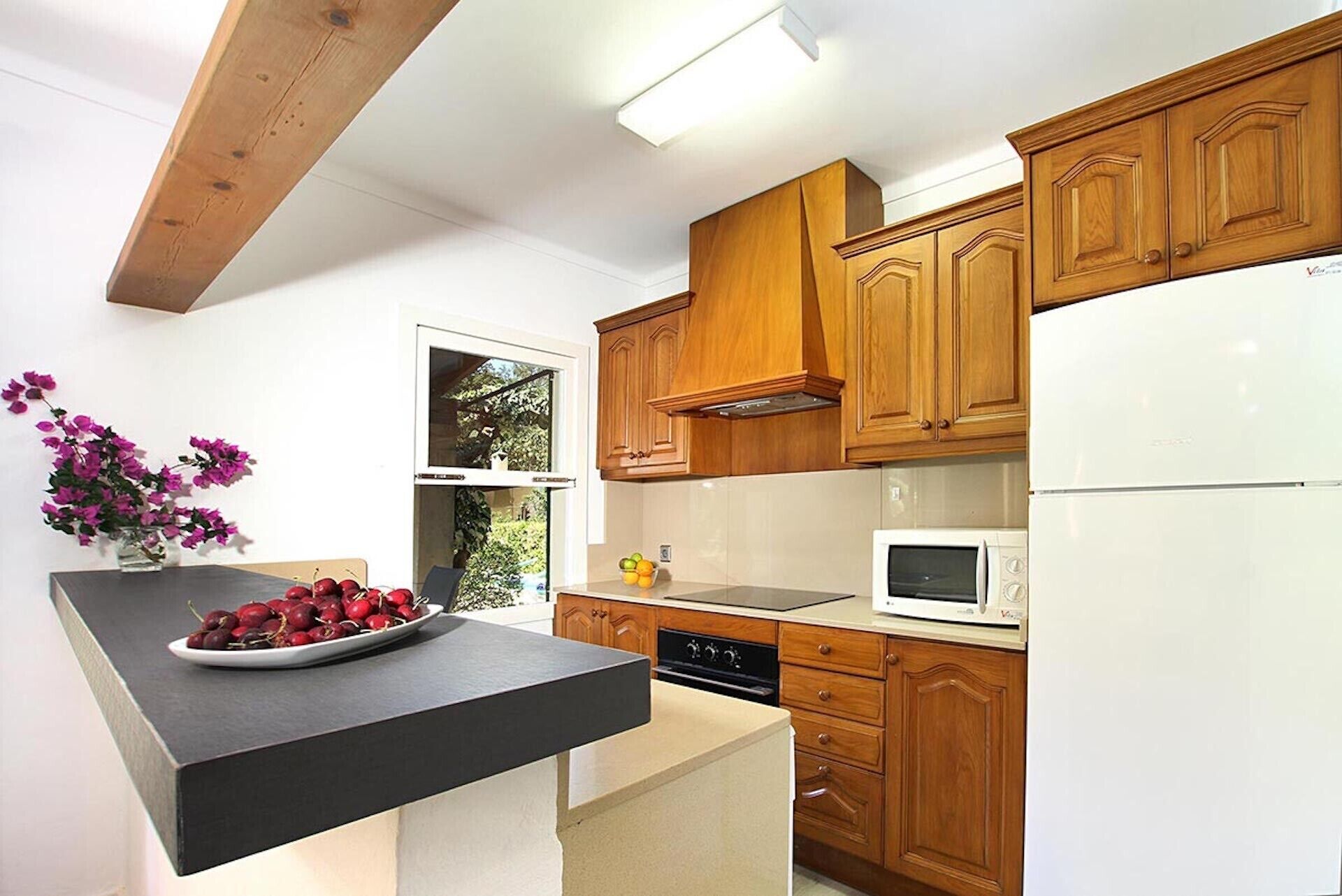 A modern kitchen with wooden cabinets, a black countertop, a white refrigerator, and a microwave.