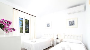 Una habitación de hotel con dos camas, un escritorio, una silla, un ventanal con cortinas y un radiador.