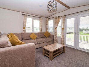 A living room with a sofa, a wooden coffee table, and curtains on large windows. - The Drift, Skipsea - A Coastal Retreat (Driffield)