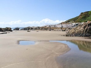 Una playa con arena, una pequeña masa de agua y terreno rocoso.