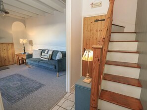 Eine Treppe mit Holzbalken und Handlauf, ein blaues Sofa mit Kissen, ein kleiner Tisch mit Lampe und ein Teppich auf dem Boden.