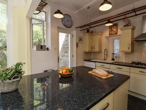 A kitchen with a black countertop, a clock, cabinets, and a window. - The Woodlands, Berrynarbor (Ilfracombe)