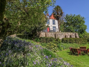 A stone building with a red roof, surrounded by lush greenery and flowering plants. - The Woodlands, Berrynarbor (Ilfracombe)