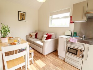 A compact living space with a kitchenette, a sofa, a dining table, and a potted plant. - Bramble - A Charming Retreat (Norwich)