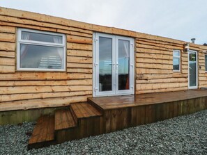 Eine Holzhütte mit einer Terrasse, einer Glastür und einem kleinen Fenster.