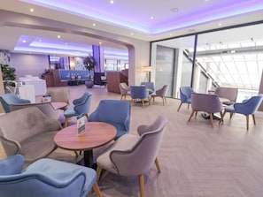 Un moderno vestíbulo de hotel con zonas de estar, un mostrador de recepción y una escalera que conduce a un nivel superior.