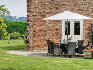 Ein Backsteinhaus mit einer Terrasse, die Korbmöbel und einen weißen Sonnenschirm zeigt.