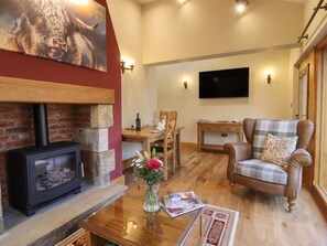 Ein gemütliches Wohnzimmer mit Kamin, einem an der Wand befestigten Fernseher, einem Karo-Sessel und einem Holztisch.