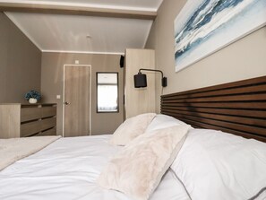 A bedroom with a bed, a dresser, a door, and a wall-mounted lamp. - 63 The Maples, Sticker, 2 bed. (St Austell)