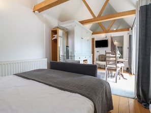A bedroom with a bed, a desk, and a television in the adjacent room. - Charming Little Barn Retreat in Orwell (Royston)