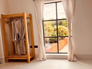 Ein Zimmer mit einem hölzernen Handtuchregal, einem großen Fenster mit Vorhängen und Blick auf einen Garten.