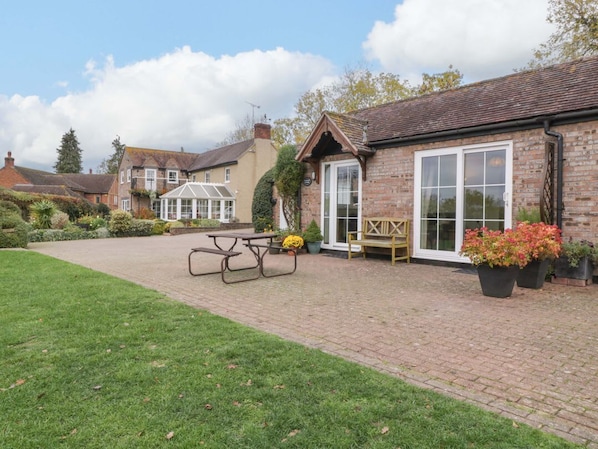 A brick building with a large glass door, a picnic table, and potted plants. - Dovecote Cottage, Gloucester (Gloucester)