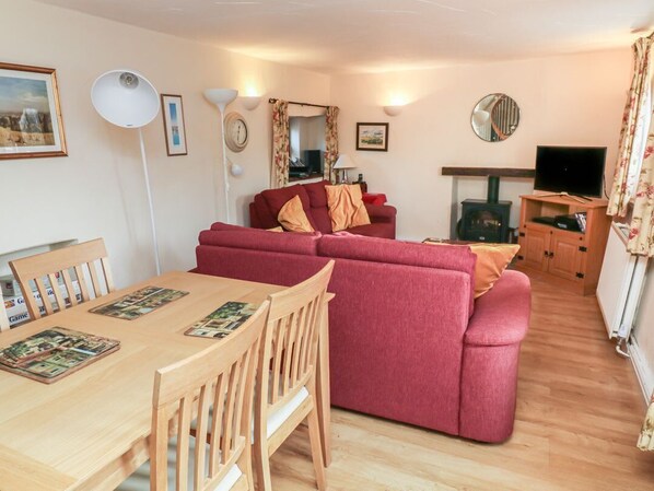 A living room with a red sofa, wooden dining table, and chairs. There is a television and a fireplace.