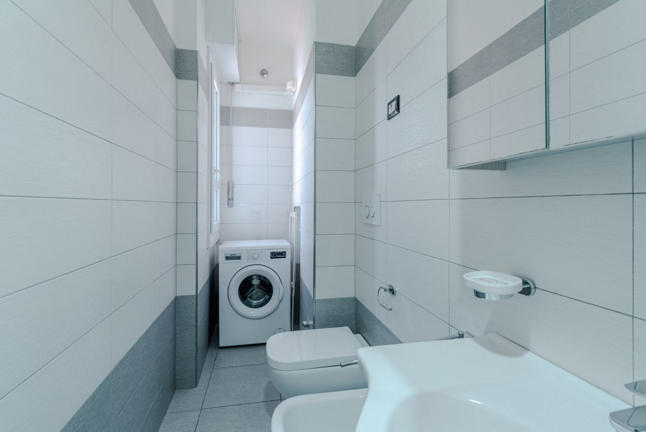 Une petite salle de bain équipée d’un lave-linge, de toilettes et d’un lavabo.