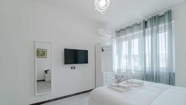 Une chambre d’hôtel moderne dotée d’un grand lit, d’un téléviseur à écran plat, d’un miroir et d’une fenêtre avec des rideaux légers.