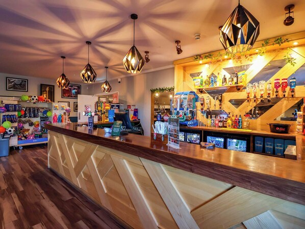 Una zona de bar con suelo de madera, una barra con diversas bebidas y lámparas colgantes.