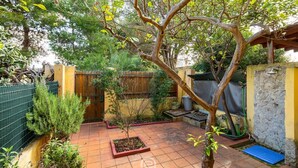 Un patio con piso de baldosas, un árbol y una pequeña zona ajardinada.