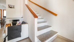 Una escalera con barandillas de madera, una pared blanca y un salón con sofá y chimenea.