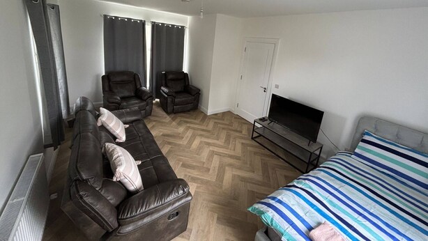 A room with a sofa, two armchairs, a TV, and a bed.
