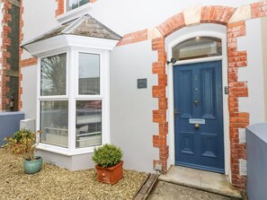 A house with a blue door, a bay window, and a brick wall. - Aubrey Villa in Pembrokeshire. (Tenby)