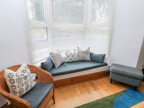 A room with a built-in bench, a wicker chair, and a small table. - Aubrey Villa in Pembrokeshire. (Tenby)