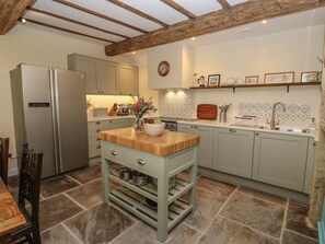 A kitchen with a central island, a refrigerator, cabinets, a sink, and a clock on the wall. - The Farmhouse, in East Morton. (Keighley)