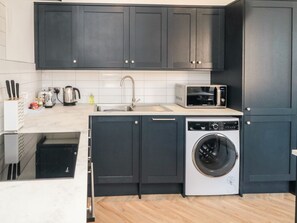 A compact kitchen with dark cabinets, a microwave, a sink, and a washing machine. - Apartment 2, Scarborough, 2bed (Scarborough)