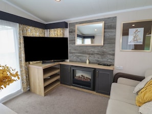 A living room with a flat-screen TV, a fireplace, a sofa, and a mirror on the wall. - Stag Lodge, Caravan 70, Belton, Norfolk (Great Yarmouth)