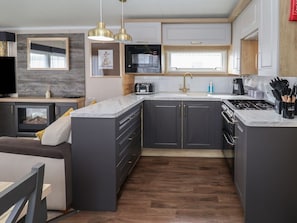 A modern kitchen with dark cabinets, a central island, a microwave, a stove, and a sink. - Stag Lodge, Caravan 70, Belton, Norfolk (Great Yarmouth)