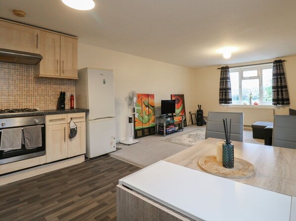 A modern kitchen with wooden cabinets, a built-in oven, a refrigerator, and a dining area with a table and chairs. - Peckhamsbest Suite, Southwark, London (London)