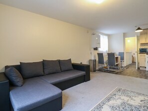 A modern living room with a grey sofa, a patterned rug, and a kitchen in the background. - Peckhamsbest Suite, Southwark, London (London)