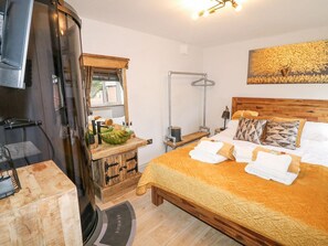 Un dormitorio con cama, cabecera de madera, mesita de noche, lámpara colgante, ventana con cortinas y una obra de arte en la pared.