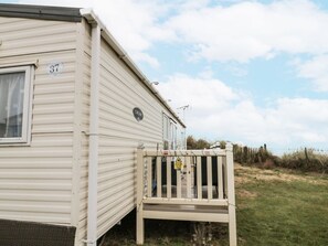A mobile home with a number '37' on the side, a small porch with a safety sign, and a grassy area in the background. - Sands Retreat at 37 Redcar Beach (Redcar)