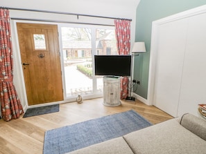 Ein Zimmer mit Holztür, einem Fernseher auf einem weißen Schrank, einer Couch und einer Lampe.